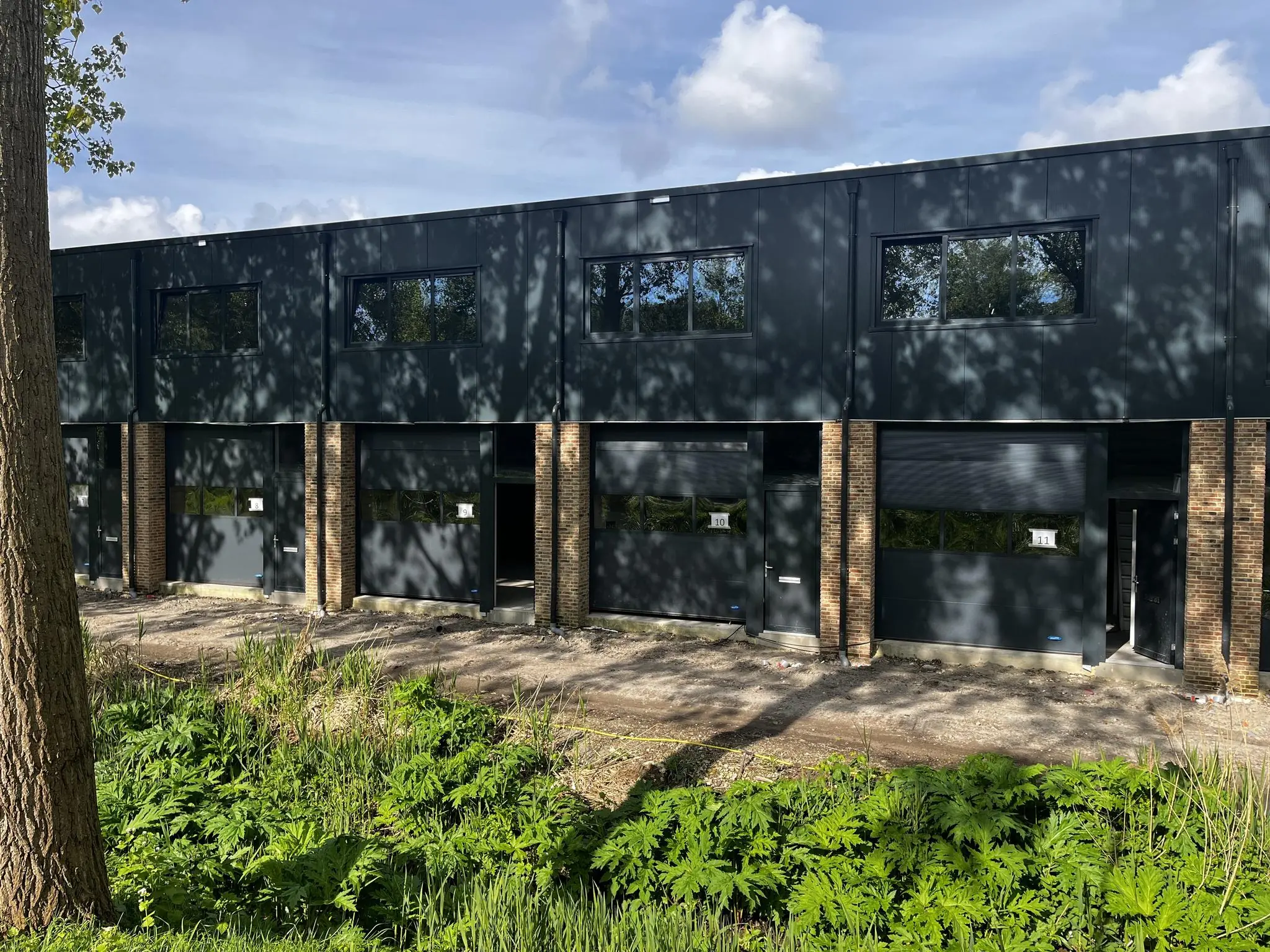 Zwarte bedrijfsunits met bakstenen pilaren aan de Broekdijk West, genummerd 10 en 11.